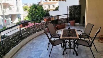Un balcón con mesa y sillas, plantas en macetas y vistas a edificios.