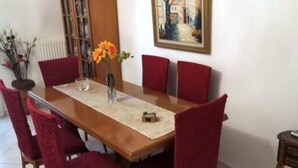 A dining area with a wooden table, red upholstered chairs, a vase with flowers, and a framed painting on the wall. - Alex’ s apartment in Trikala (Trikala)
