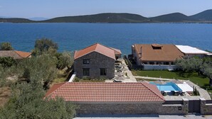A coastal property with stone buildings, a swimming pool, and a view of the sea and hills.