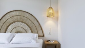 Cama com cabeceira de fibra trançada, mesa de cabeceira com um livro e óculos, e luminária pendente.