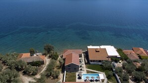 Vista aérea de uma propriedade costeira com piscina, vários edifícios e uma vista desobstruída do mar.