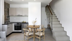Una cocina moderna con armarios blancos, una pared de acento de piedra, un rincón comedor con una mesa redonda y sillas, y una escalera con barandilla de metal.