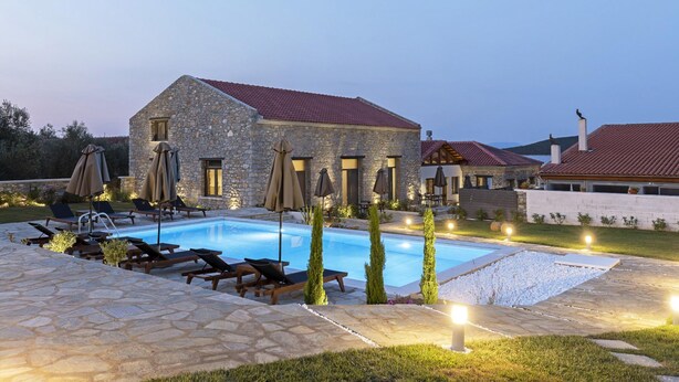 Un edificio de piedra con piscina, sillas de descanso y sombrillas.