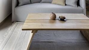 Un salon moderne avec un mur en pierre, un canapé gris, une table basse en bois et une fenêtre donnant sur un bâtiment au toit rouge.