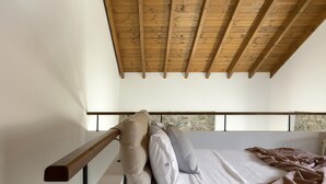 Une chambre avec un plafond en bois, un lit avec des oreillers et un mur en pierre derrière le lit.