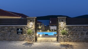 A stone-walled entrance to a property named LICHNOS, with a pool and a view of hills in the background. - Lichnos Luxury Suite (Sourpi)