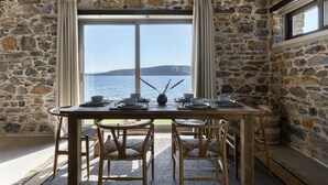A stone-walled dining area with a table set for four, overlooking a body of water. - Lichnos Luxury Suite (Sourpi)