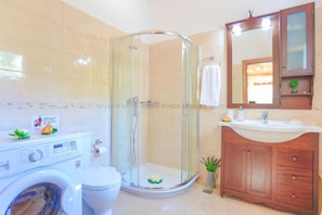 Une salle de bain avec une douche à parois de verre, un lave-linge, des toilettes et un meuble-lavabo en bois avec un miroir.