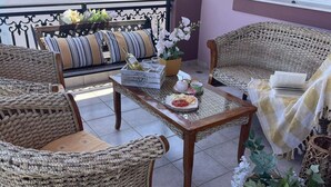 A cozy outdoor seating area with wicker furniture, a table with a bottle and glasses, and a potted plant. - Aithrea's Homes in Pastida Rhodes (Pastida)
