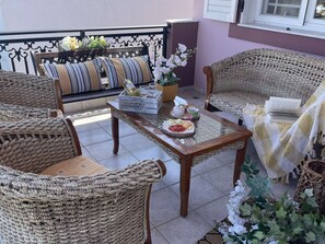 A cozy outdoor seating area with wicker furniture, a table with a bottle and glasses, and a potted plant. - Aithrea's Homes in Pastida Rhodes (Pastida)