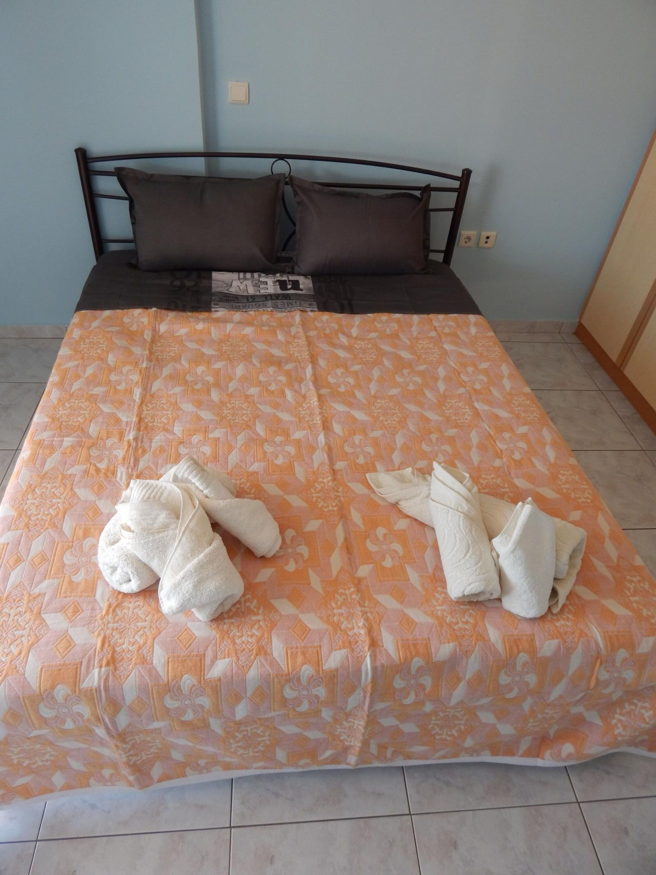 A neatly made bed with a patterned bedspread and two towels folded on it.