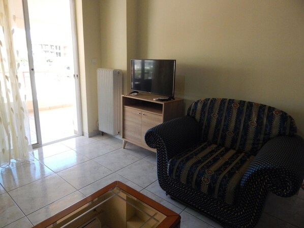 A living room with a sofa, a television on a wooden stand, and a glass coffee table.