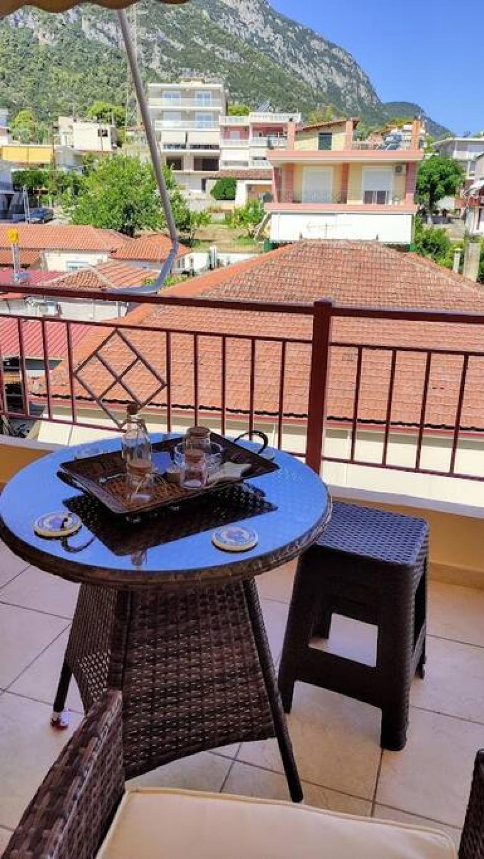 A balcony with a round table and two chairs, overlooking a mountainous area with buildings.