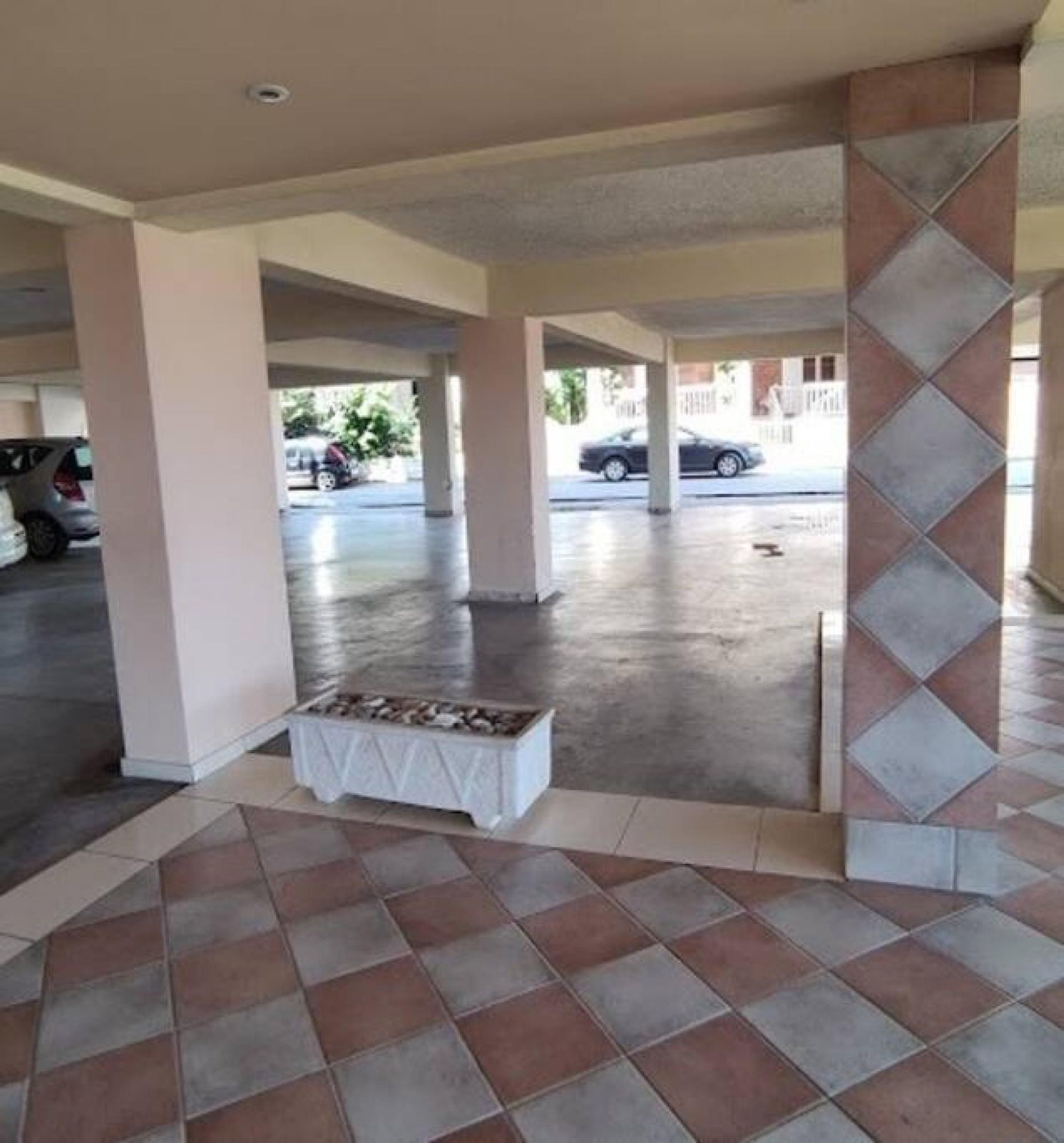 A covered outdoor area with tiled flooring, a fire pit, and a view of parked cars and buildings in the background.