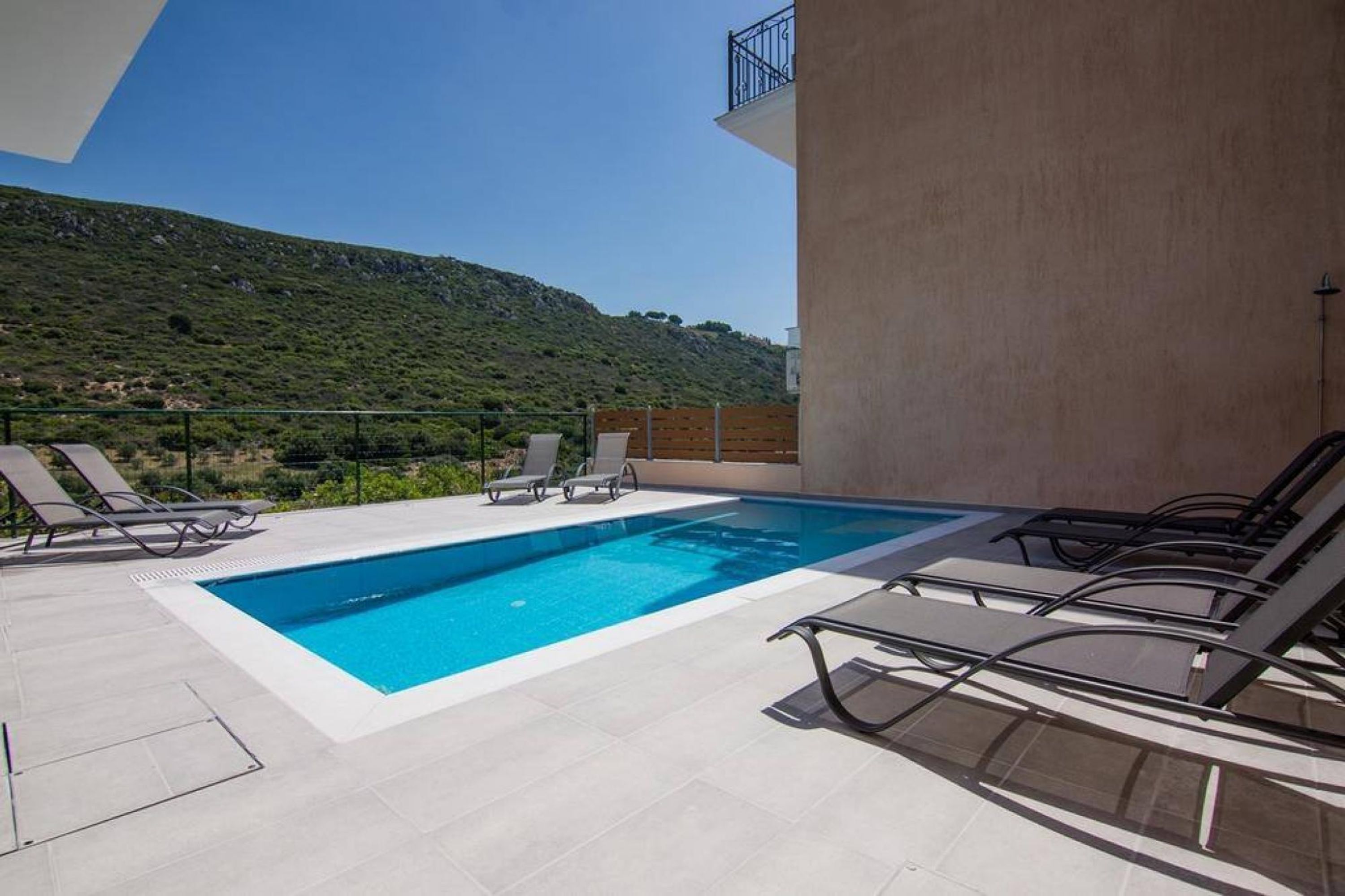 Une piscine sur le toit, avec une eau d’un bleu cristallin, entourée de chaises longues, et offrant une vue sur une colline verdoyante.