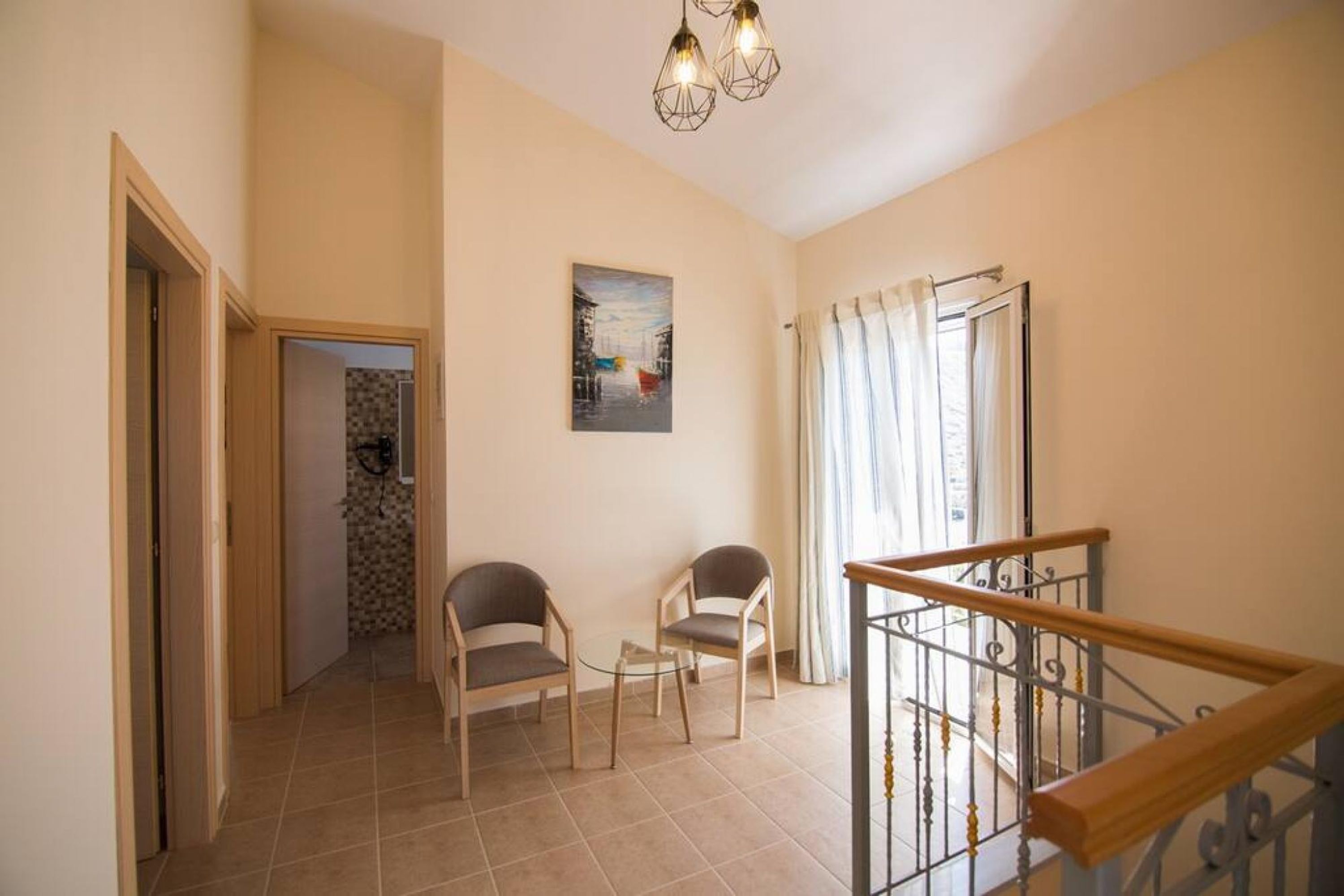 Un hall d’entrée spacieux avec un escalier, deux chaises, une petite table et un tableau accroché au mur.