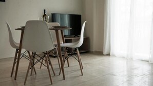Zona de menjador amb taula i cadires, un televisor i una finestra amb cortines.