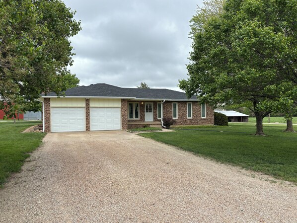 A single-story house with a brick facade, two garage doors, and a gravel driveway.
