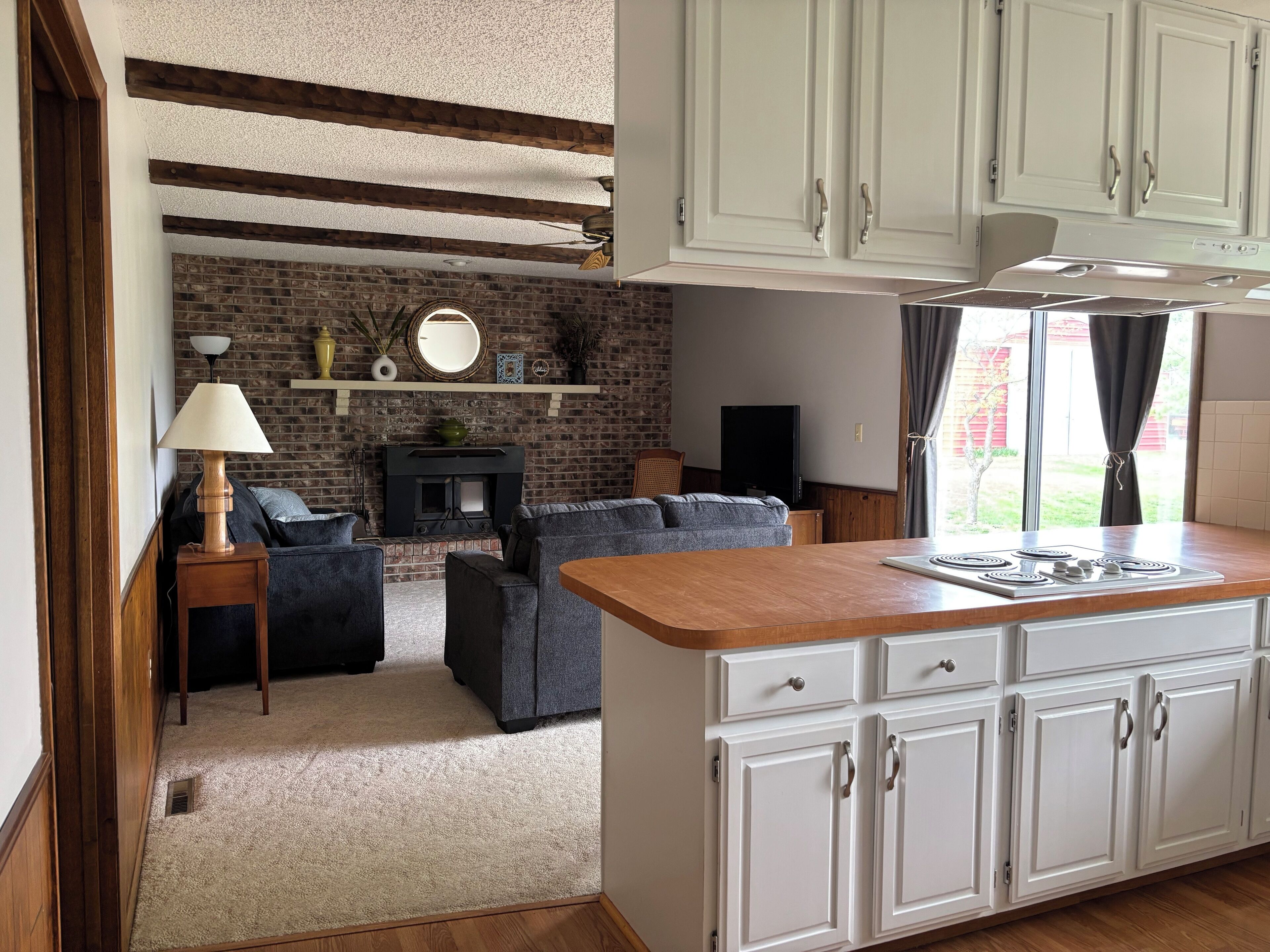 A kitchen with white cabinets, a wooden countertop, and a brick wall.