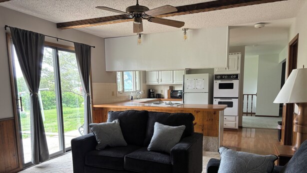 Uma sala de estar moderna com um sofá escuro, uma mesa de centro de madeira e vista para uma cozinha e área de refeições.