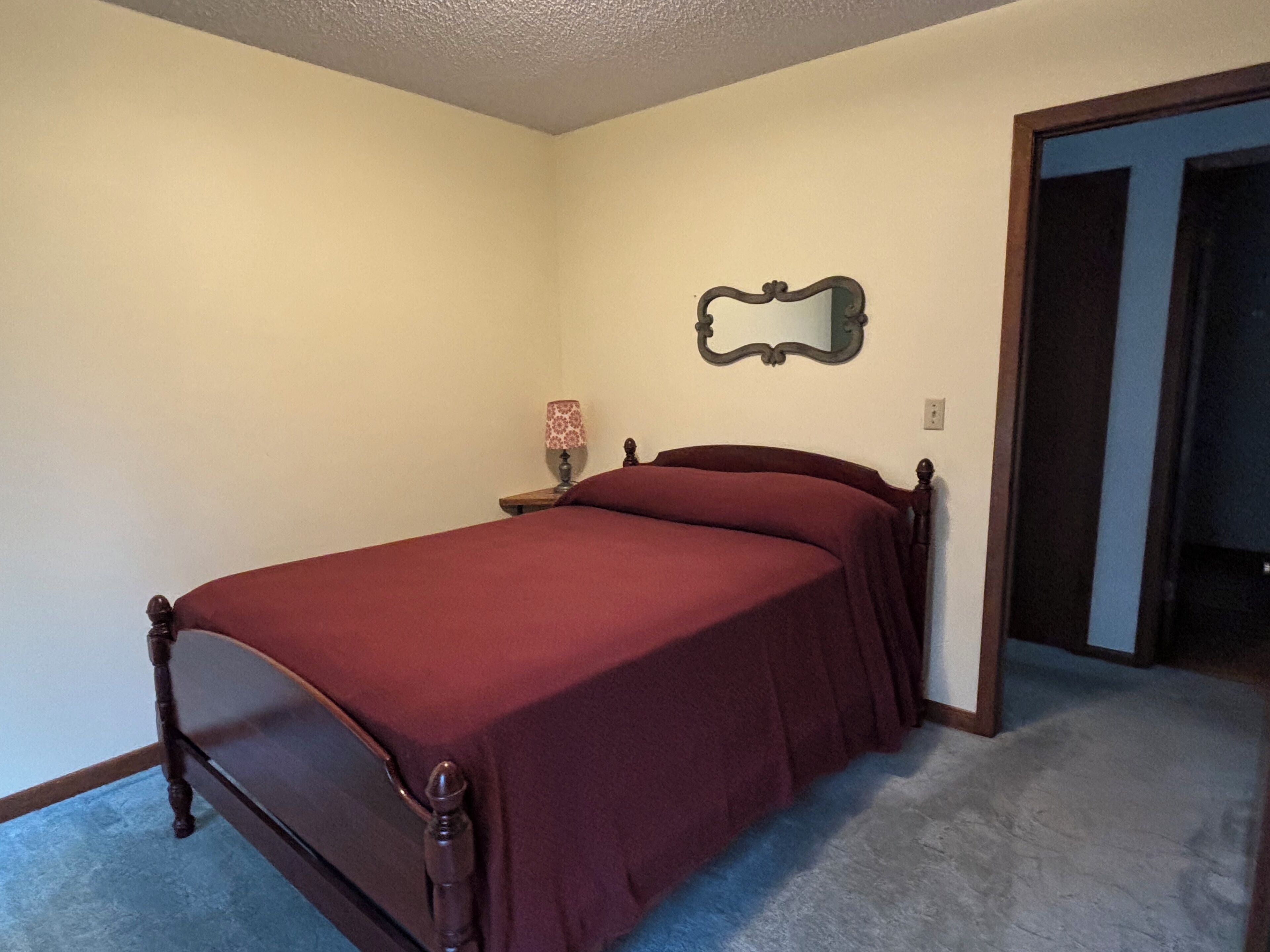 A bedroom with a bed, a nightstand, a lamp, and a mirror on the wall.