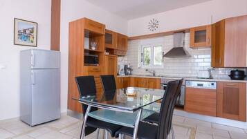 Eine moderne Küche mit Holzschränken, einem Glastisch und einem Edelstahlkühlschrank.