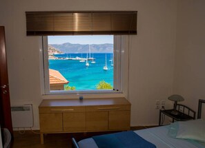 Een slaapkamer met een groot raam met uitzicht op een jachthaven en bergen.