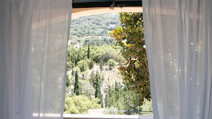 A balcony with a table and chairs, a view of a green landscape, and white curtains. - Myrtos Cottages Polimnia (Divarata)