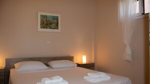 A neatly made bed with white linens and towels, a bedside table with a lamp, and a painting on the wall. - Myrtos Cottages Polimnia (Divarata)