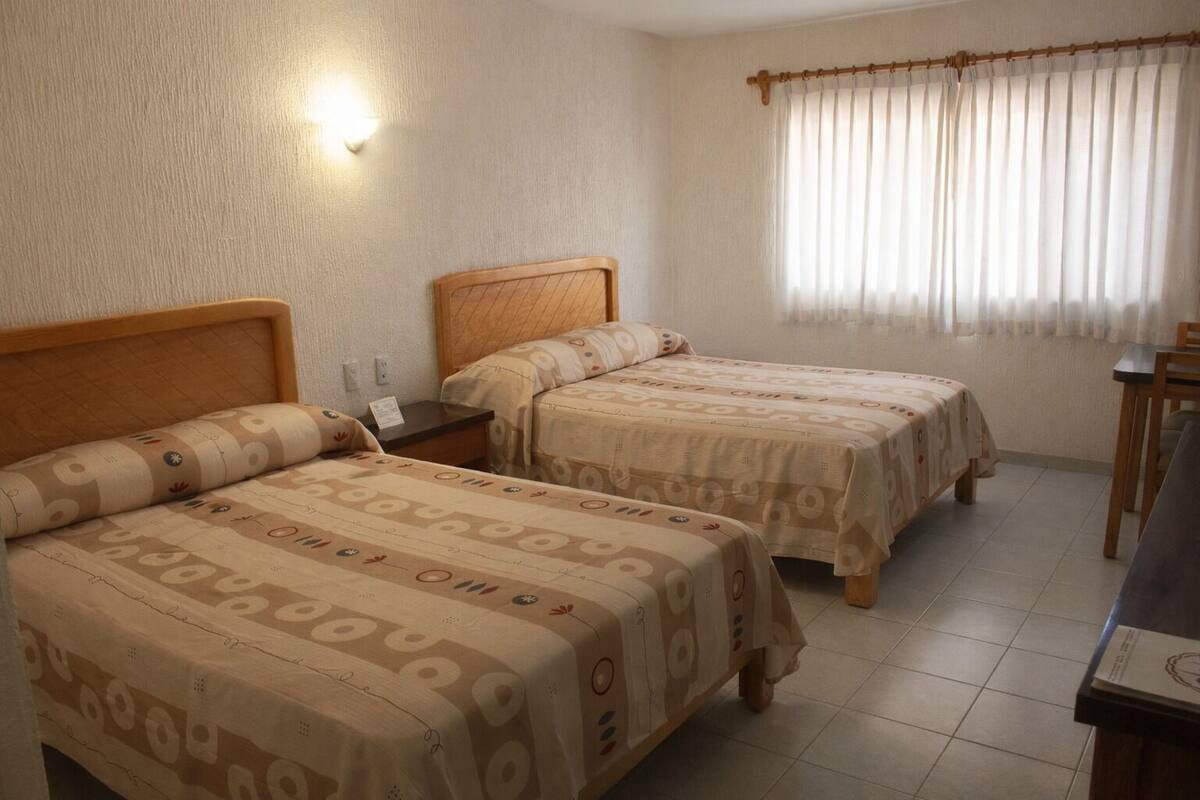 Ett hotellrum med två sängar, ett skrivbord, en stol och ett fönster med gardiner.
