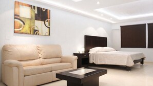 A modern hotel room with a sofa, a bed, a nightstand, and a large abstract painting on the wall.