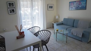 A living room with a sofa, a glass coffee table, a dining table with chairs, and a window with curtains.