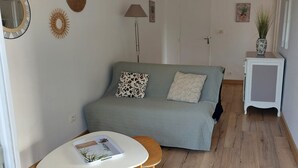 Um quarto acolhedor com um sofá cinzento, uma mesinha de cabeceira branca e um chão de madeira.