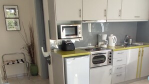 A modern kitchen with white cabinets, a microwave, a coffee maker, and a kettle. There is a blue sofa in the living area.