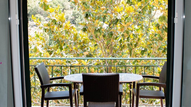 Un balcon avec une table et des chaises, une vue sur les arbres et un sol carrelé.
