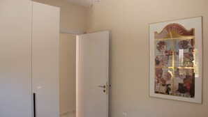 Un couloir avec une porte blanche, une œuvre d’art encadrée au mur et un sol carrelé.
