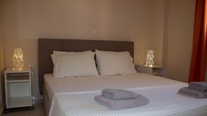 Un lit bien fait, avec du linge de lit blanc et deux oreillers, une table de chevet avec une lampe, et une serviette pliée posée sur le lit.