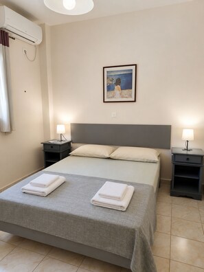 A hotel room with a bed, two bedside tables with lamps, a painting on the wall, and an air conditioning unit.