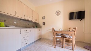 Een keuken met beige kastjes, een eettafel met vier stoelen, een klok aan de muur en een flatscreen tv die boven de tafel is bevestigd.
