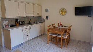 Een keuken met lichte kastjes, een houten eettafel met vier stoelen, een witte hanglamp en een flatscreen televisie aan de muur.