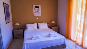 Un lit bien fait, avec du linge de lit blanc et deux serviettes pliées, une table de chevet avec une lampe et un tableau encadré au mur.