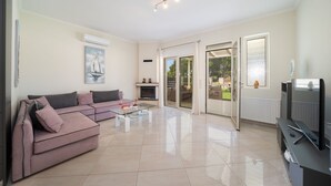 A modern living room with a sectional sofa, a glass coffee table, a flat-screen TV, and a fireplace. - Averto Apartment at Skala (Eleios-Pronnoi)