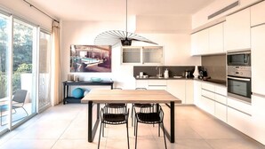 A modern kitchen with white cabinets, a wooden dining table, and black chairs. - Hovevei Tsiyon Magnolia (Tel Aviv-Yafo)