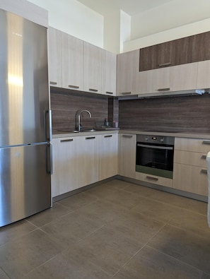 Une cuisine moderne avec des meubles en bois clair, des appareils électroménagers en acier inoxydable et un four encastré.