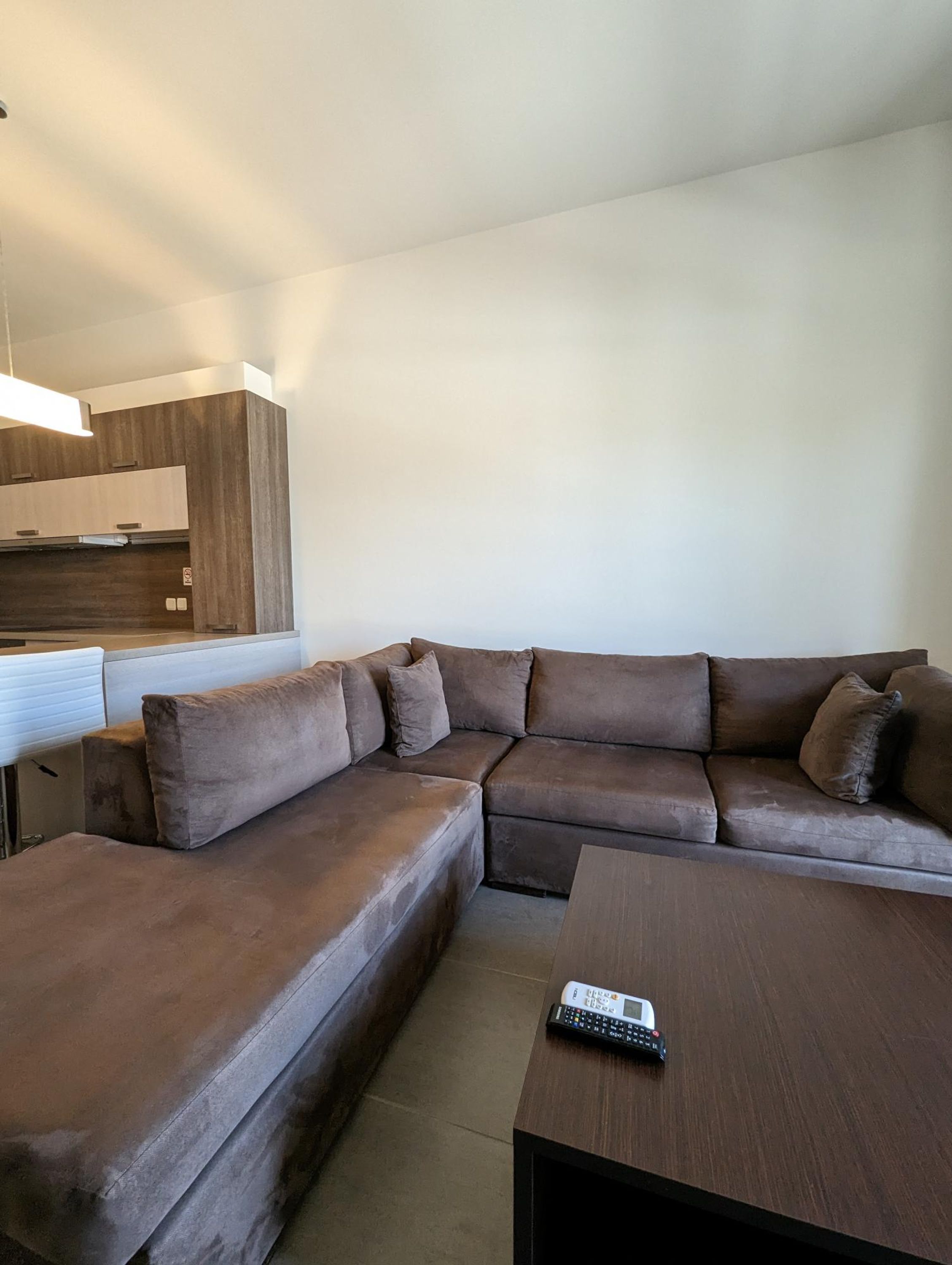 A modern living room with a sectional sofa, a coffee table, and a kitchen area in the background.