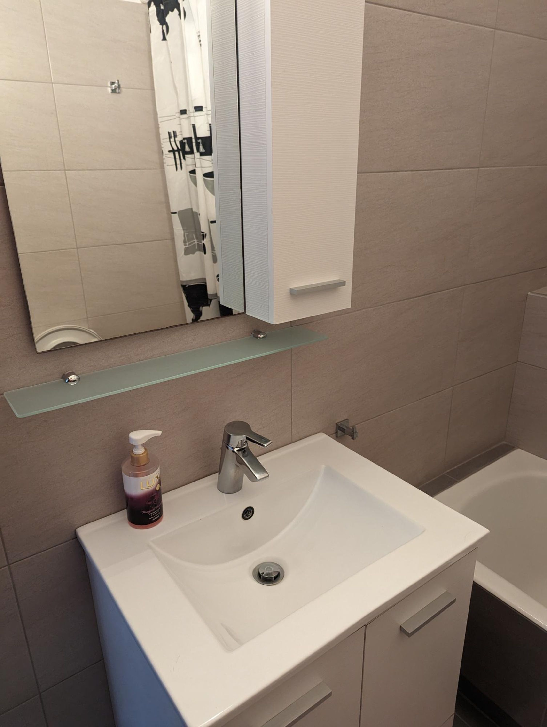 A bathroom with a white sink, a mirror, and a glass shelf above it.