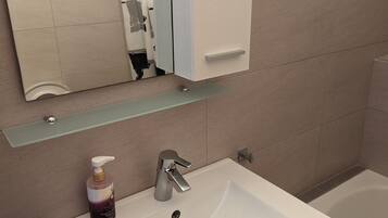 A bathroom with a white sink, a mirror, and a glass shelf above it.