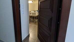 A hallway with a wooden door leading to a room with a white ceiling and a hanging light fixture. - Samaras Apartments Le Grand (Kamena Vourla)