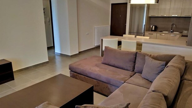 A modern living room with a sectional sofa, a coffee table, and a dining area with a table and chairs. - Samaras Apartments Le Grand (Kamena Vourla)