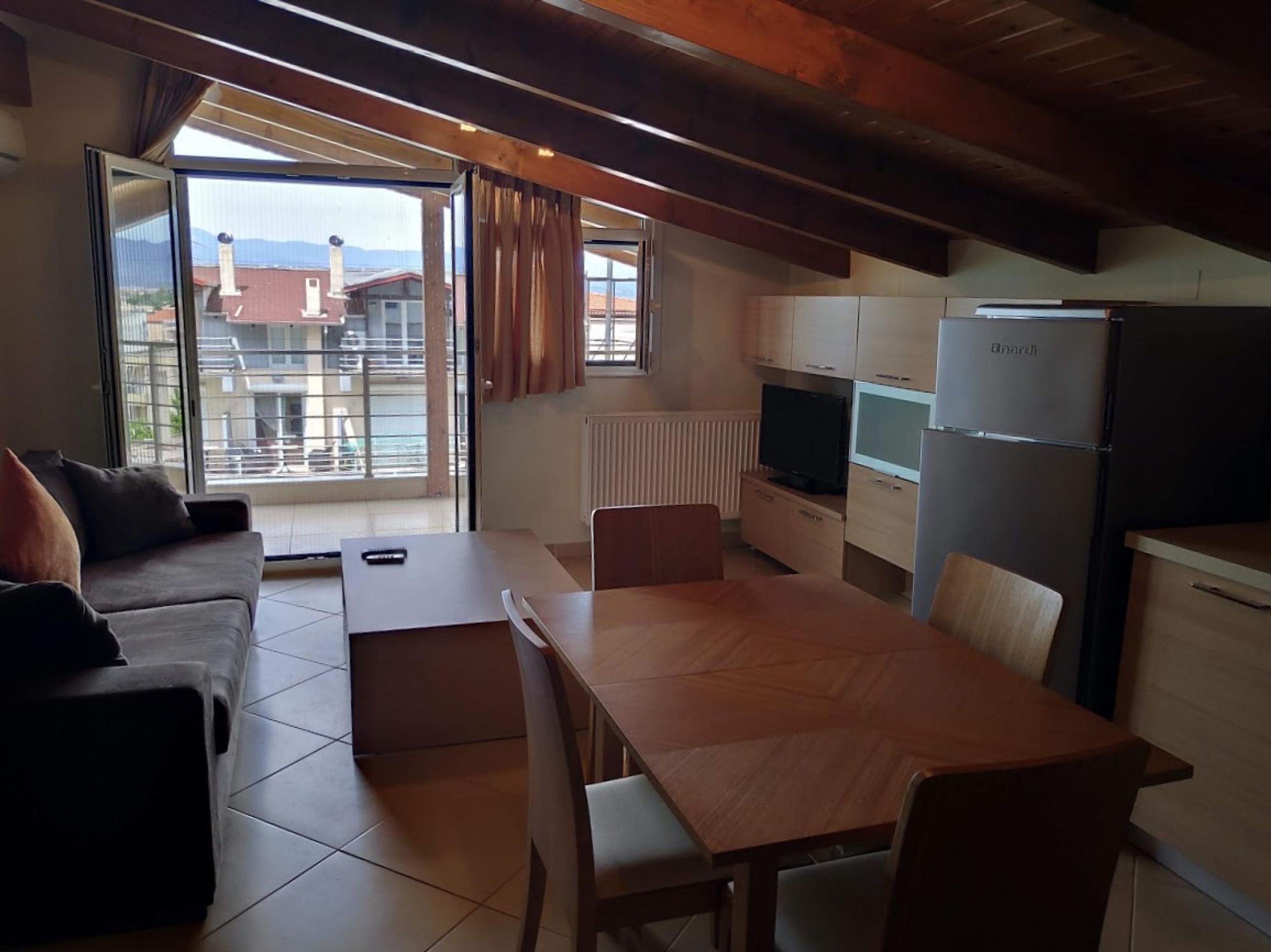 A compact living space with a sofa, a dining table, a TV, and a kitchen area including a refrigerator and a microwave.